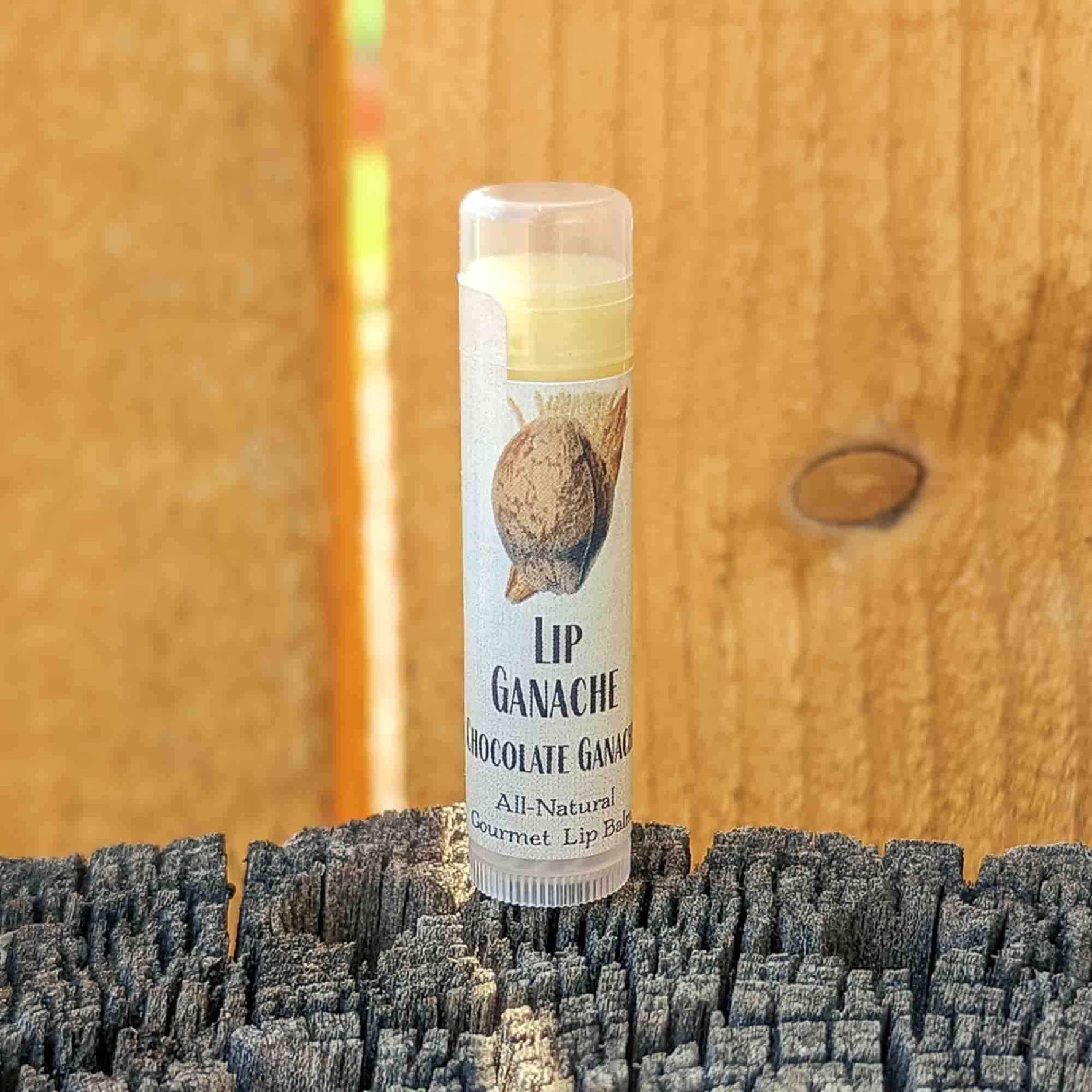 Tube of Lip Ganache Chocolate Ganache lip balm standing on a weathered wood post against a cedar fence