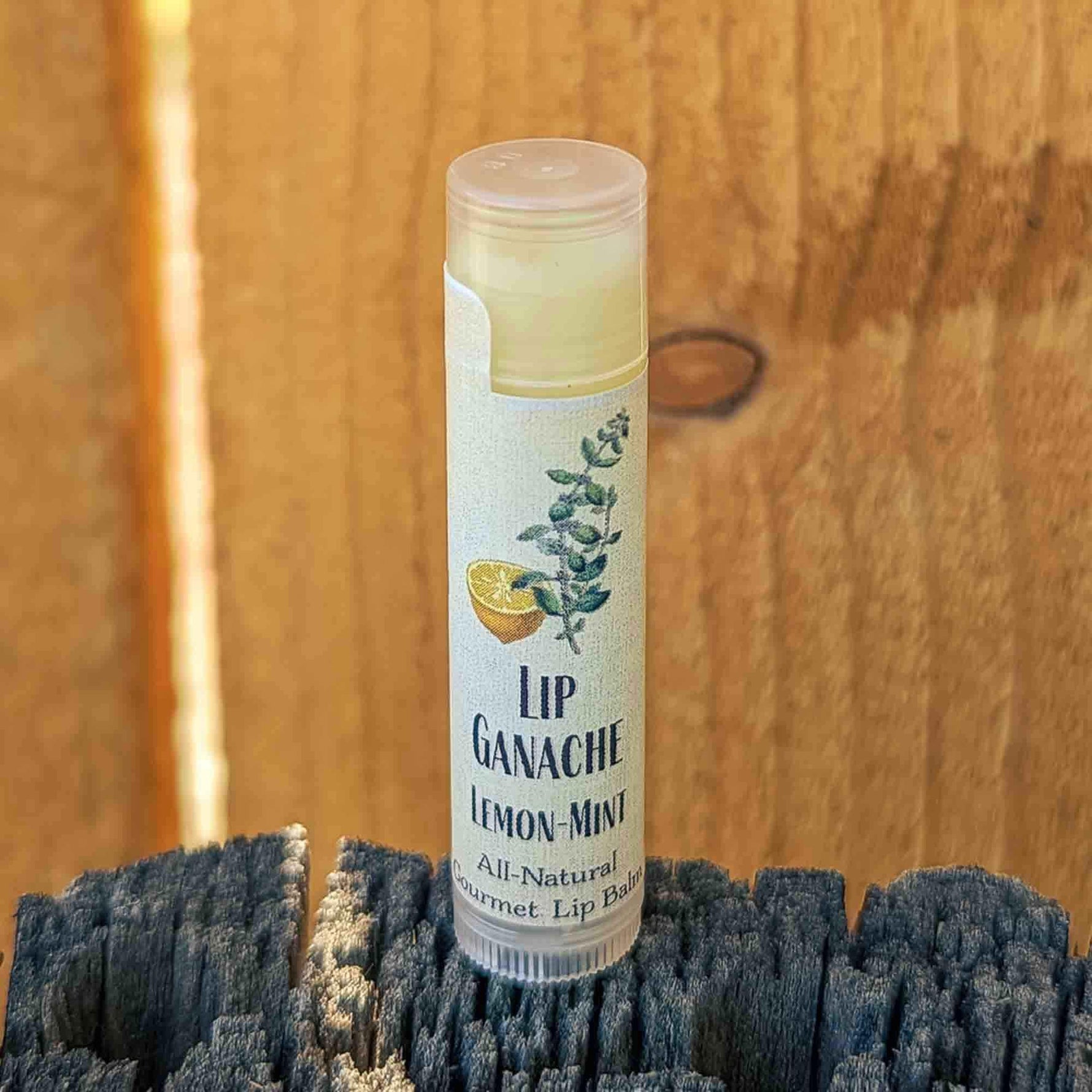 Tube of Lip Ganache Lemon Mint lip balm standing on a weathered wood post against a cedar fence