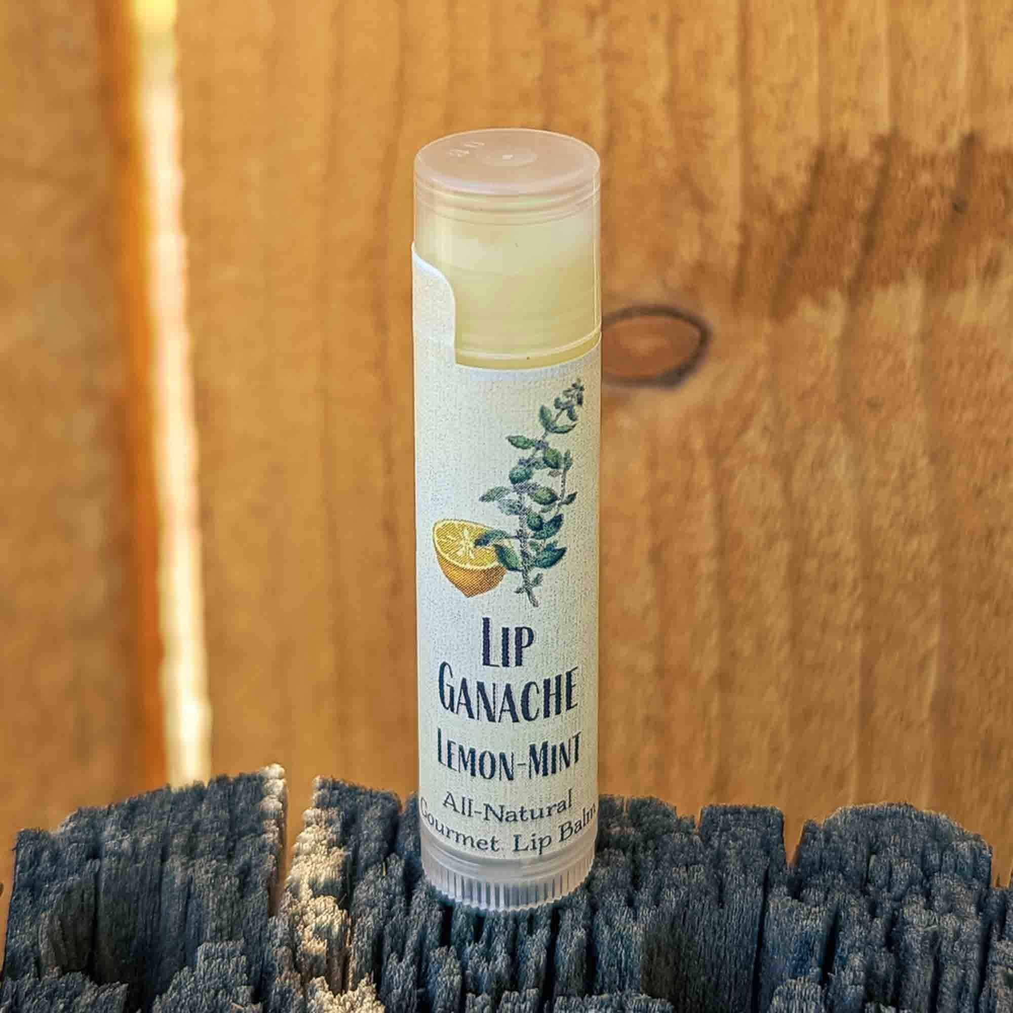 Tube of Lip Ganache Lemon Mint lip balm standing on a weathered wood post against a cedar fence